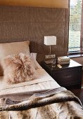 Bedroom in natural shades - fur cushion and cosy blanket on double bed with wide, upholstered headboard