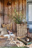 Young birch twigs in wicker basket on rope rug and printed cushions on animal skin rug