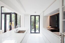 Minimalistische, weiße Kücheninsel auf dunkel gerahmte Terrassentüren
