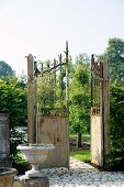 Rustic iron gate leading to well-tended garden with trees and paved path