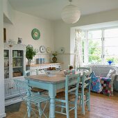 Cosy, cottage-style kitchen-dining room with old dining table painted pastel blue and wicker sofa with colourful patchwork blanket