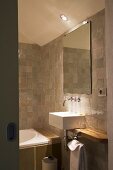 Blick durch offene Tür ins Designerbad mit Waschbecken und Wandarmatur unter Spiegel an gefliester Wand