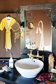 Waschtisch mit Waschschüssel vor Spiegel und im Hintergrund aufgehängter Bademantel an Stellwand
