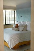 Blick durch Türöffnung auf Doppelbett mit Kissenstapel vor hellblauer Wand