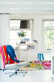 Colourful towel on swivel chair and white, modern dining area with bright kilim rug in background