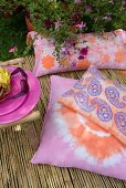 Batik-patterned and Paisley-print cushions on bamboo mat in summer garden