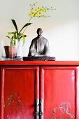 Statuette next to yellow orchid in pot on half-height, Oriental-style, red lacquer cabinet