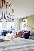 Designer Hängeleuchte aus Holzlamellen über Esstisch vor Butterfly Sessel und schwarze Ledersofagarnitur in minimalistischem Wohnraum