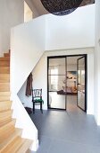 Offenes, modernes Treppenhaus mit Holztreppe und grauem Steinboden im Foyer, offene Glastür und Blick in Wohnraum