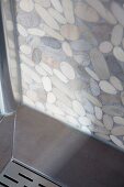 Ecke einer Duschkabine mit Abdeckplatte für Wasserablauf und Duschwand im Terrazzo-Look