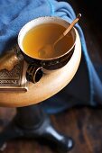 Braune Keramiktasse mit heißem Tee und Plätzchen auf Hocker