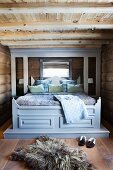 Fur rug on floor in front of rustic double bed with grey-painted canopy frame in bedroom in log cabin