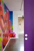 Blick durch offene, violette Tür in modernen Gang mit bunter Graffitibemalung an Wand
