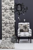 Roll of Toile de Jouy wallpaper on black wall next to armchair; black pendant lamp in foreground