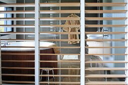 Blick durch Raumteiler mit Holzlamellen auf runde Wellnesswanne in Bad Ensuite