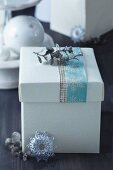 Festive gift box with pastel snowflake-patterned ribbon and silver, glittery leaves