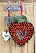 Heart made of leaves and rosehips and metal hearts hanging on hooks on wooden wall