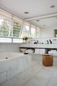 White marble bathroom with mirrored wall above washstand and angled exterior blinds on windows along one side