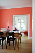Dark wooden chairs at antique dining table in room with walls painted salmon pink and wide doorway