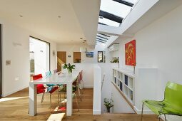 White dining table and colourful plastic chairs in open-plan kitchen with skylight