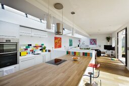 Kitchen counter with pale wood worksurface and bar stools in open-plan interior