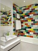 Bathroom with washstand and mirrored cabinet next to bathtub against wall with colourful tiles