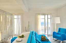 Mediterraner Wohn- Schlafraum mit blauen Polstermöbeln im Loungebereich und Tisch mit Hocker vor Himmelbett