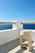 Wooden stool in corner of roof terrace below blue sky with view of sea