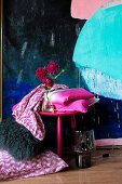 Gefaltete Bettbezüge auf pinkfarbenem Hocker vor modernem Gemälde