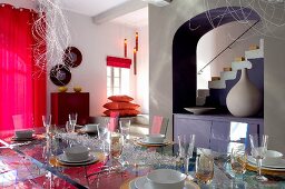 Festively set table in open-plan, modern interior with view of staircase through archway painted purple
