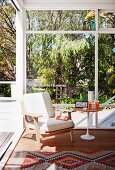 Gemütlicher Lesesessel neben Designertisch vor großer Glasfront mit Blick in den sommerlichen Garten