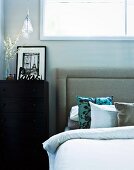 Black and white photo of Paris on black chest of drawers next to double bed with upholstered headboard and silk scatter cushions