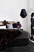 Black bed with decorative cane headboard and luxurious fur blanket in elegant bedroom with anthracite woollen rug and black pendant lamp