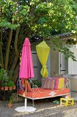 Metall Tagesbett im Garten neben geschlossenem, pinkfarbenem Sonnenschirm und an Baum aufgehängtem gelbem Baldachin