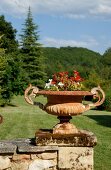 Planted metal urn on stone wall in front of wooded landscape