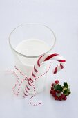 Candy cane tied to glass of milk next to holly berries