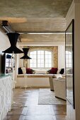 View into loft-style interior with window seat in niche and designer standard lamps with black lampshades below exposed concrete ceiling