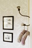 Padded coat hangers on antique hook with glass knobs; framed drawings on wallpapered wall
