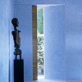 African sculpture on pedestal in blue foyer with view into garden through sliding wooden door