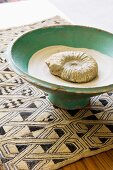 Ammonit mit Sand in Keramikschüssel auf gemusterter Webdecke