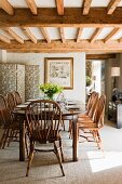 Country-house-style dining room with tasteful wooden furniture below wood-beamed ceiling; floral screen in corner
