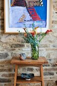 Farbenfrohes, modernes Gemälde an rustikaler Natursteinwand; davor ein kleiner Wandtisch mit einem prächtigen Callastrauss