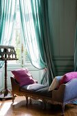 Rococo recamier with velvet upholstery and scatter cushions next to music stand in front of window with draped, airy curtains