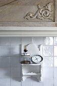 White-painted, Oriental-style wall bracket on white-tiled wall below wall unit with carved details on wooden door