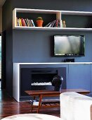 Einbauelemente im Farbmix Anthrazit und Weiß mit Kamin neben Sideboard, Regalfach und Fernseher gegenüber Sofa