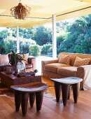 Sitzecke mit Sofa, afrikanischen Holzhockern & Couchttisch in Wohnraum mit geöffneten Schiebetüren zum Garten