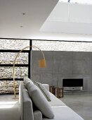 Pale grey sofa in front of wooden designer arc lamp in contemporary interior with open fireplace in exposed concrete wall