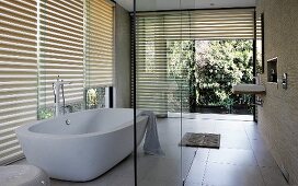 Designer bathroom with free-standing bathtub in front of glass wall with half-closed louver blinds