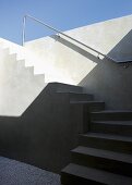 Minimalist, winding, exterior concrete staircase with stainless steel handrail on wall below a blue sky