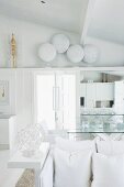 View past white cushions on bench to collection of white-painted shields on shelf above door in white designer interior
